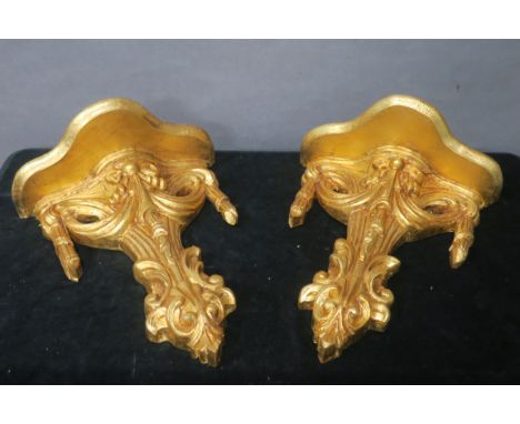 A PAIR OF NEO CLASSICAL STYLE GILT WALL MOUNTED BRACKETS, the serpentine shaped shelf above a ribbon tied and foliate base,48