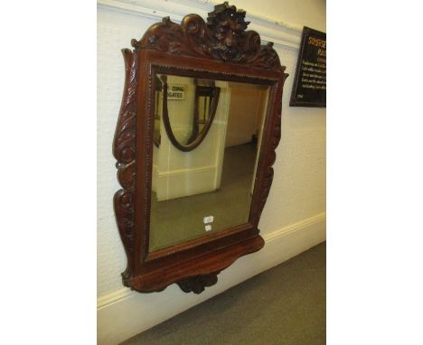 Early 20th Century wall mirror with all over floral carved and maskhead decoration with single shelf and bevelled edge plate