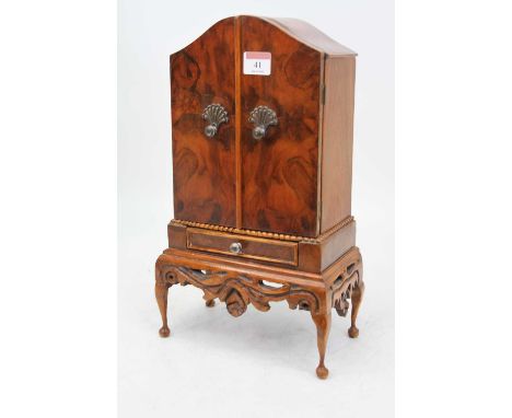 A miniature walnut table top cabinet in the style of a Queen Anne cabinet on stand, with arched top and twin doors opening to