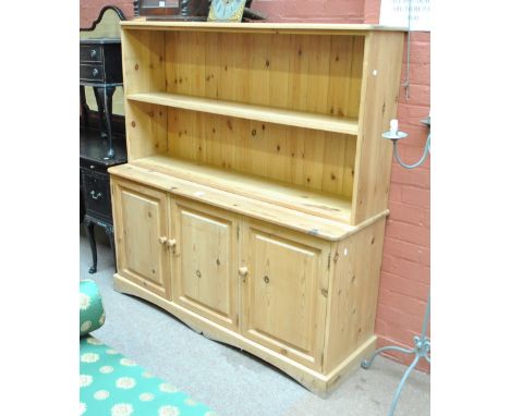 A modern pine bookcase, the upper section having a single shelf above a base of three cupboard doors.