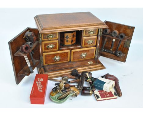 An oak smokers' cabinet, the hinged doors and lid enclosing an octagonal tobacco jar decorated with ivy leaf motifs and a qua