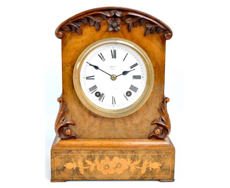 A Victorian walnut eight day mantel clock, the floral carved frame centred with a white enamel dial set with Roman numerals a