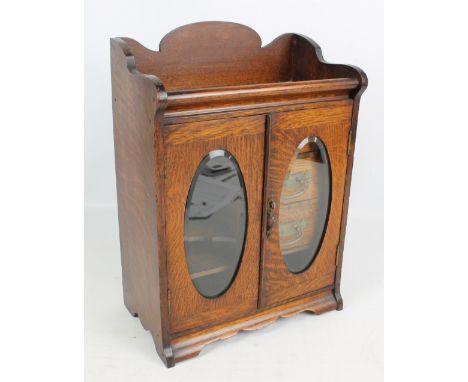 An Edwardian oak smokers' cabinet with pair of glazed door enclosing three drawers, a tobacco compartment with pipe rack abov