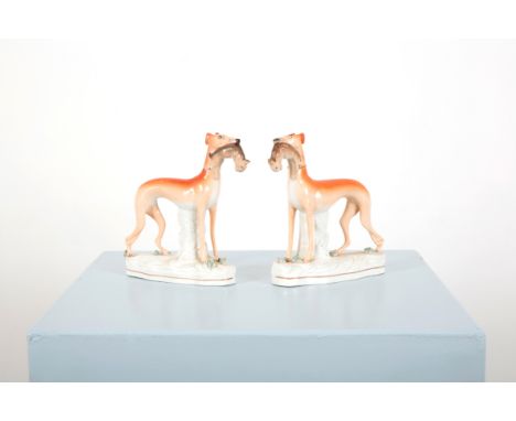 A PAIR OF STAFFORDSHIRE STANDING GREYHOUND FIGURESlate 19th century, posed with rabbits in their mouths, on gilt lined shaped