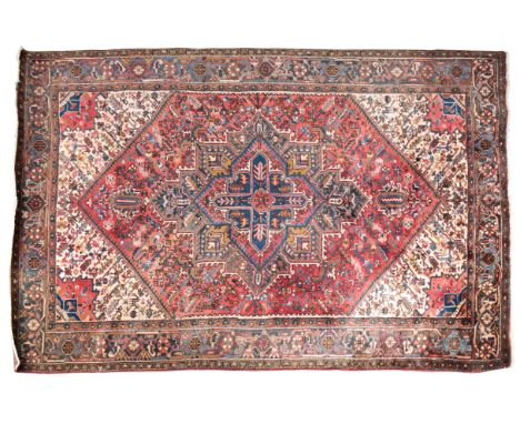 A HERIZ PERSIAN CARPETwoven in muted colours and off-white with star-shaped medallion and angular spandrels on a madder groun