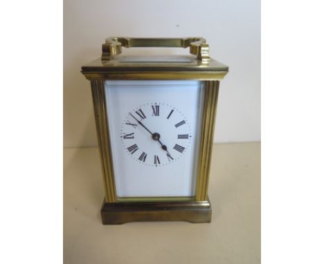 A brass carriage clock with glazed sides and top panels, of white enamel dial and Roman numerals, 13cm high, with handle down