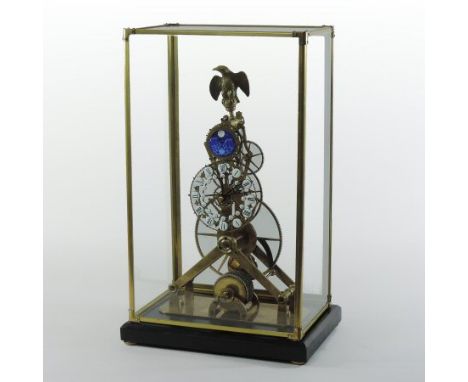 A brass skeleton clock, having enamel hours and a moonphase, surmounted by an eagle, on an ebonised plinth, in a glazed displ