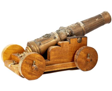 A 19th Century Victorian scaled down size carved oak model cannon having a reeded barrel with applied brass lion masks and mi