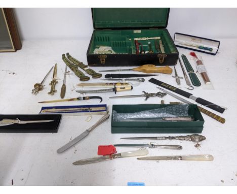 A collection of vintage paper knives, small ornamental daggers and a silver plate meat skewer, contained in a leather clad cu