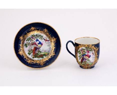 A Worcester blue ground coffee-cup and saucer, painted with reserves of exotic birds in branches, and landscape and buildings