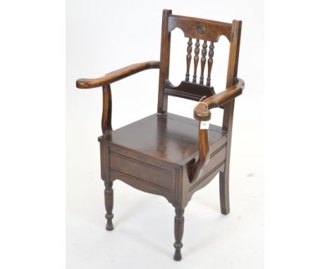 A Victorian oak commode chair, with turned spindle back and outswept arms above a hinged seat enclosing a commode and raised 
