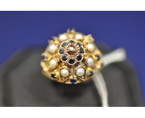 A sapphire and half pearl dress ring, the central "boss" surrounded by sapphires and half pearls on a yellow metal shank, rin