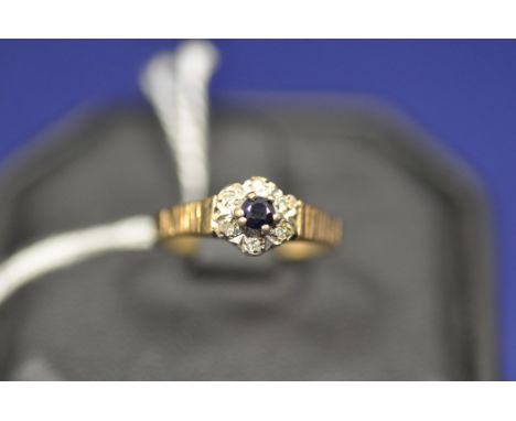 Sapphire and diamond cluster ring flanked by textured shoulders on a 9ct. yellow gold shank, ring size L.