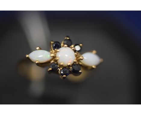 An opal and sapphire ring, the central circular opal cabouchon flanked by marquise cut opal cabochons, surrounded by six circ