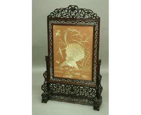 A CHINESE FIRESCREEN the pierced hardwood frame on carved lion feet, enclosing a panel with silk embroidered peacock height 5