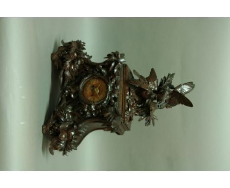 A BLACK FOREST MANTEL CLOCK the walnut case carved with birds fighting and leafy branches, wooden dial with brass numerals, m