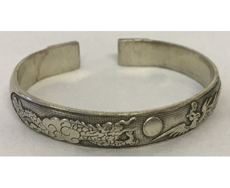 A Chinese white metal bangle with dragon and phoenix detail.  