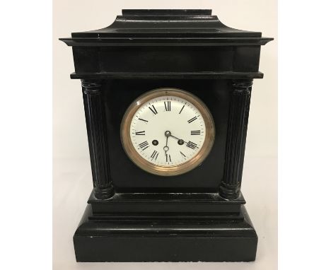 A Victorian black slate mantle clock with column detail. Enamelled face with roman numeral markers and bevel edged glass. Com