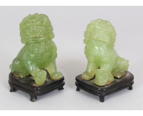 A PAIR OF 20TH CENTURY CHINESE CELADON JADE-LIKE HARDSTONE MODELS OF BUDDHISTIC LIONS, together with fixed wood stands, 3.25i
