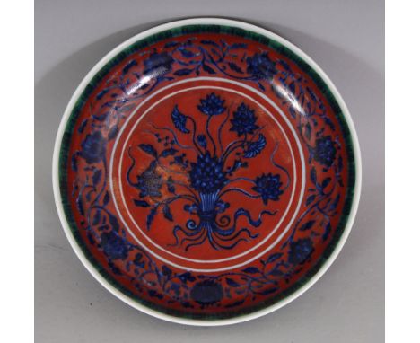 A CHINESE MING STYLE RED GROUND BLUE & WHITE LOTUS BOUQUET PORCELAIN SAUCER DISH, the rim with a narrow green classic scroll 