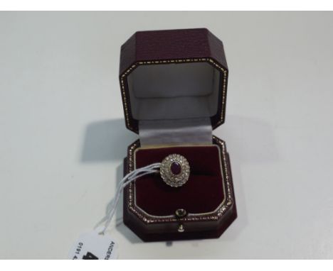 A ruby and diamond cluster ring, the oval facet cut ruby surrounded by two borders in shaped mount, on a yellow metal shank, 