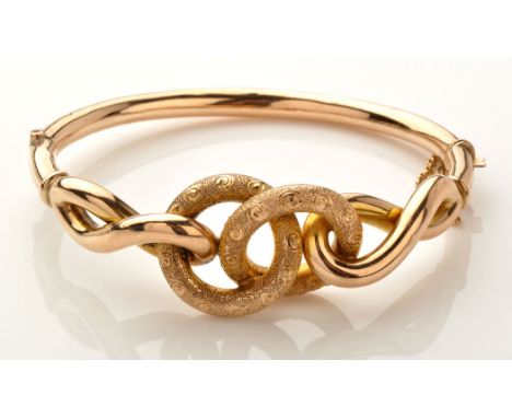 A 9ct. knot pattern bangle, hollow cast, the two entwined loops of textured design, with twist pattern shoulders, plain backs