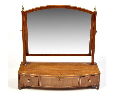 A Georgian mahogany swing frame toilet mirror, raised on reeded uprights with brass finials, the bowfront box base below fitt