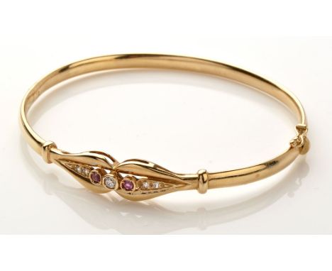 A 9ct. yellow gold, diamond and red stone bangle, the central brilliant cut diamond flanked by circular facet cut red stones 