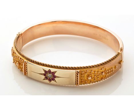 A 9ct. yellow gold Etruscan style bangle, centred by an old cut diamond, surrounded by eight red stones, in a star cut mount,