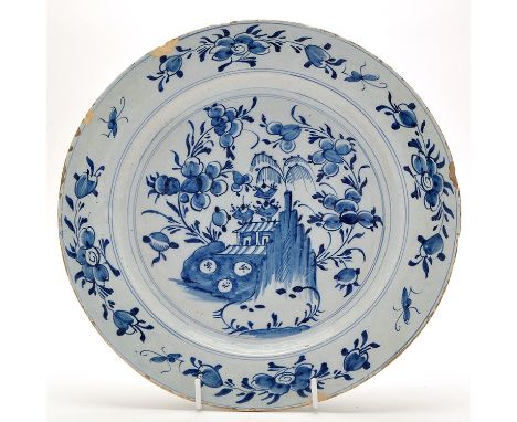 Delftware blue and white dish, painted with flowering plants and landscape beyond, enclosed by flattened rim with floral burs