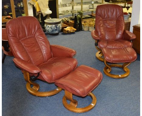 A pair of contemporary stressless adjustable red leather armchairs with matching stools by Ekorness, the frame veneered in li