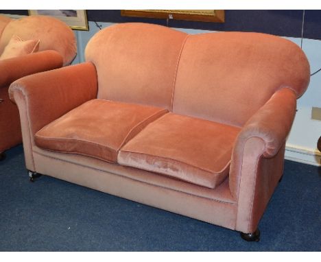 A vintage two seater sofa, upholstered in later pink velour, raised on bun feet, 82cm high x 150cm wide