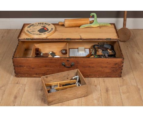 A pine bed storage box containing various items including a large cheese mixing spoon, a walking stick, a rolling pin, a carv