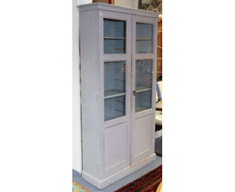 A light grey painted wooden tall cabinet fitted ten shelves enclosed by a pair of glazed panel doors, &amp; on a plinth base,