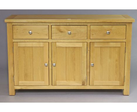 A modern light oak sideboard fitted three frieze drawers above cupboards enclosed by three panel doors 136.75cm wide x 85cm h