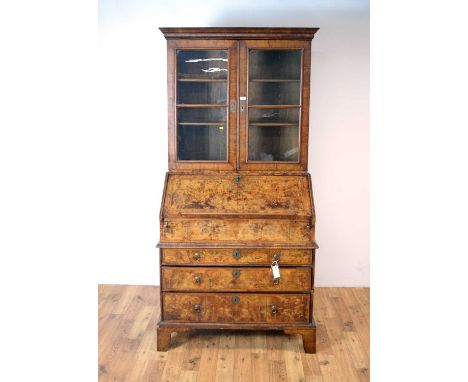 A Queen Anne burr walnut bureau with later bookcase top, the upper section with ogee cornice over two astragal glazed doors e