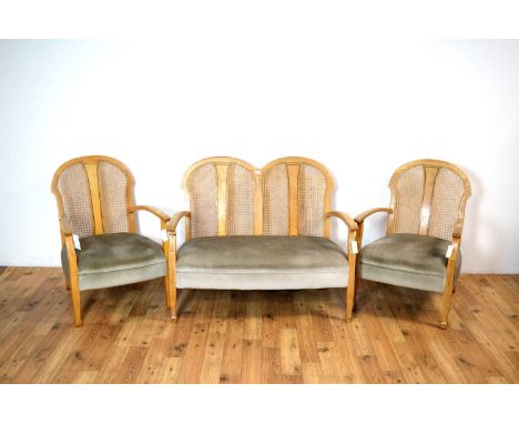 An early 20th century three-piece bergère suite, the arched rattan backrest flanked by curved elbow rests, cushioned seats ra