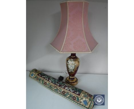 An ornate red glass table lamp with shade and a hanging tapestry 