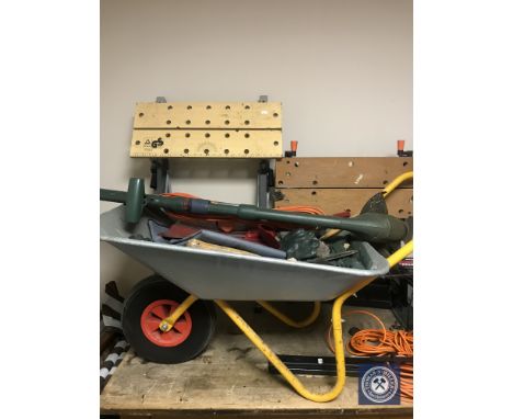 A wheel barrow containing assorted tools, gloves, electric strimmer, two folding work benches 