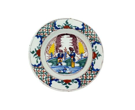 A Bristol delftware plate  mid 18th century, boldly painted with two figures standing between conical yellow trees, the rim w