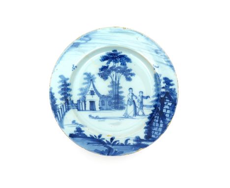 A London delftware plate  c.1770-80, painted in blue with a couple promenading between buildings beneath tall sponged trees, 