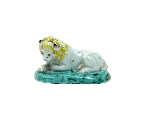 A Continental faïence model of a lion 18th century, recumbent with his front paws crossed and head lowered, on a low oval bas