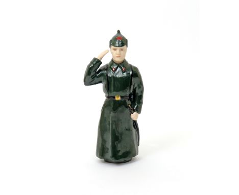 A Soviet Russian porcelain figure 20th century, of a Red Army soldier in full uniform, saluting with his right hand and holdi