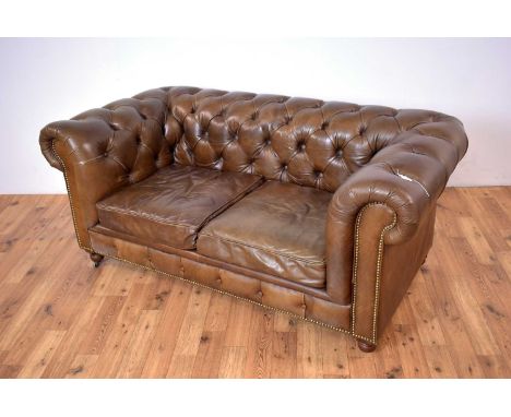 A modern brown leather Chesterfield sofa, with scrolled elbow rests, raised on turned feet and castors, 190 x 95 x 80cm high