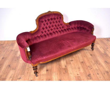 A Victorian walnut framed button back sofa, with an inlaid cresting rail over a back and seat upholstered in a red patterned 