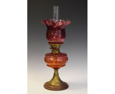 Late 19th/early 20th Century oil lamp having cranberry glass reservoir and shade, on brass flared foot on turned circular woo
