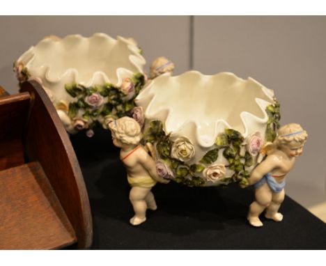 A pair of Sitzendorf flower-encrusted tripod baskets with putti supports, 23cm diameter approx.