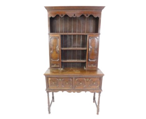 An early 20thC cottage style oak dresser, the outswept pediment over a backed three shelf plate rack, flanked by cupboards an