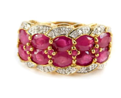A 9ct gold ruby and diamond ring, set with ten rubies in two rows, flanked by diamond set curls in a  four row pleated design