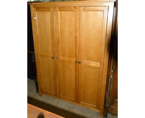 A good quality reproduction light oak triple door wardrobe, having three panelled doors with hanging rail and single base she